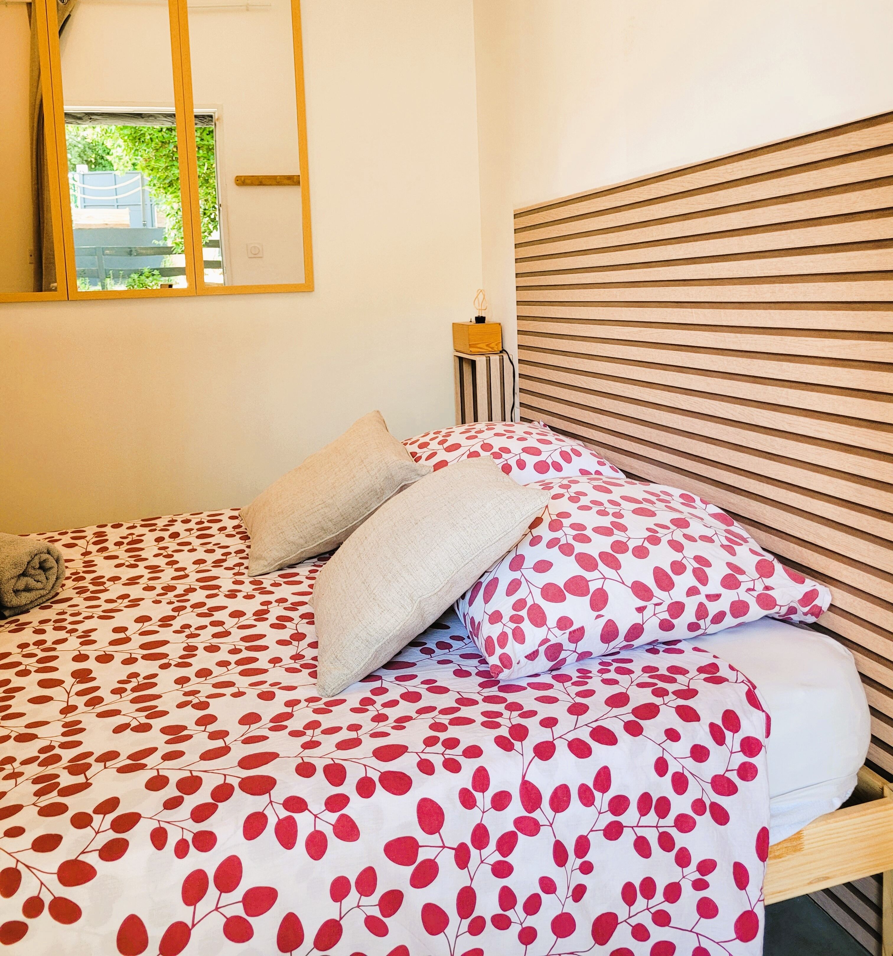 Un lit bien fait, avec une couvre-lit à motifs, une tête de lit en bois et une table de chevet sur laquelle se trouve une lampe.