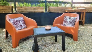 Two orange chairs with floral cushions, a small table, and a decorative bowl on a gravel surface, with a wooden fence and greenery in the background. - Allegria Nimes (Nîmes)
