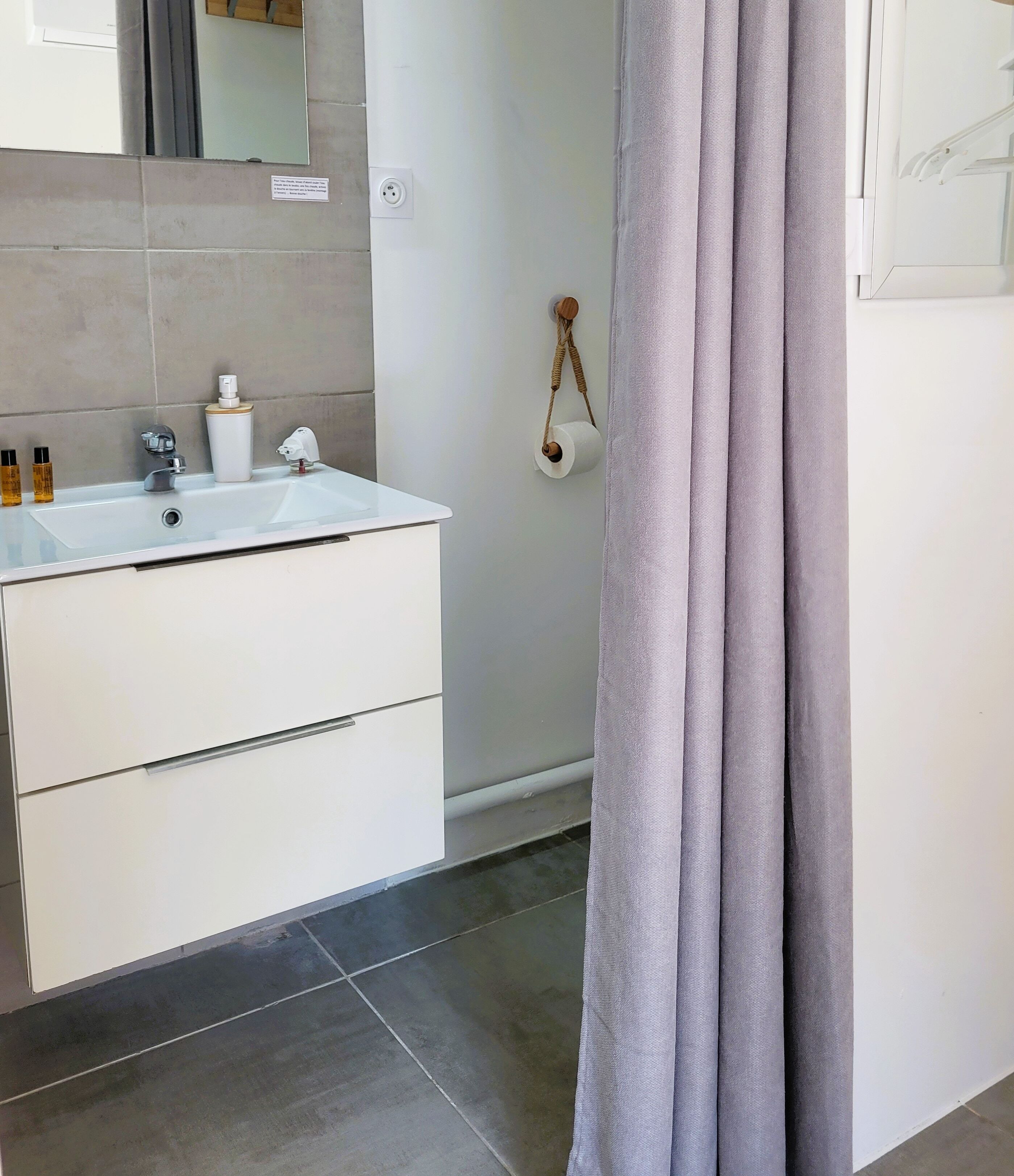 Une salle de bain avec un lavabo blanc, des articles de toilette, un miroir et un porte-serviettes.