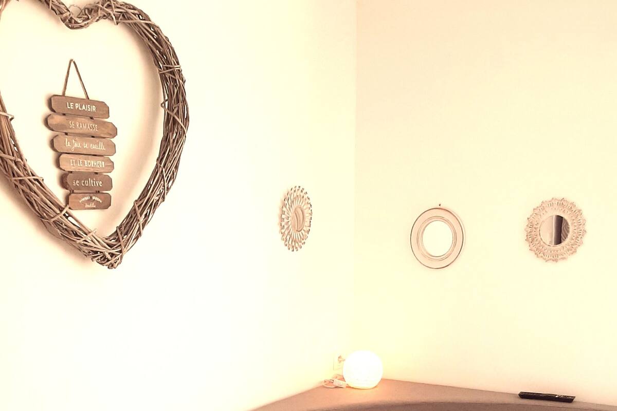 A bedroom with a heart-shaped wall decoration, a bed with patterned bedding, and two wall-mounted mirrors.