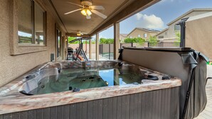 Un patio couvert équipé d’un jacuzzi, d’un ventilateur de plafond et offrant une vue sur les maisons voisines.