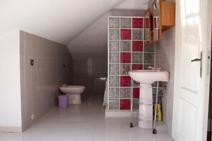 Une salle de bain comprenant des toilettes, un bidet et un lavabo, avec des murs carrelés et une porte dotée d’une poignée.