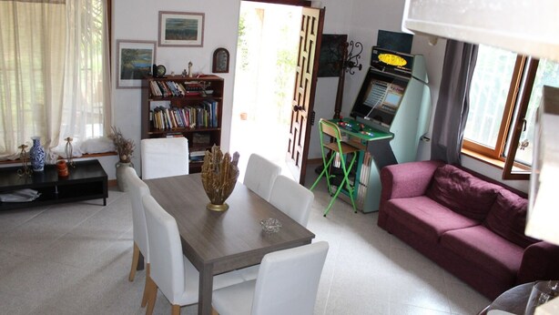 Un salon comprenant une table à manger, des chaises, un canapé, une bibliothèque et une console de jeux.
