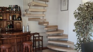 A spiral staircase with wooden steps leading to an upper level, a bar area with stools and bottles, and a potted plant. - Portion of a villa within walking distance of Mondello. (Palermo)