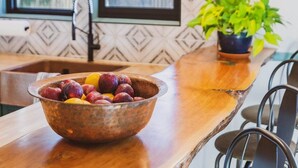 A wooden dining table with a bowl of fruit, a potted plant, and a window with a geometric patterned wall.
