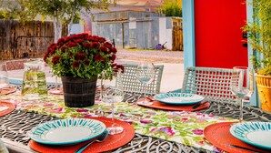 An outdoor patio with a round table set for dining, surrounded by wicker chairs.