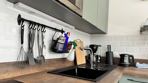 Eine Küche mit einem schwarzen Spülbecken, einer Holz-Arbeitsplatte und verschiedenen Küchenutensilien, die an einem Gestell hängen.