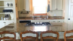 Una cocina con una isla central, muebles blancos y una ventana con persianas.
