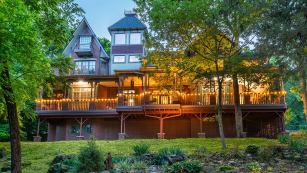 A large, two-story house with a balcony and a stone wall in the foreground. - Angel At Rose Hall (Eureka Springs)