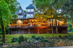 A large, two-story house with a balcony and a stone wall in the foreground. - Angel At Rose Hall (Eureka Springs)