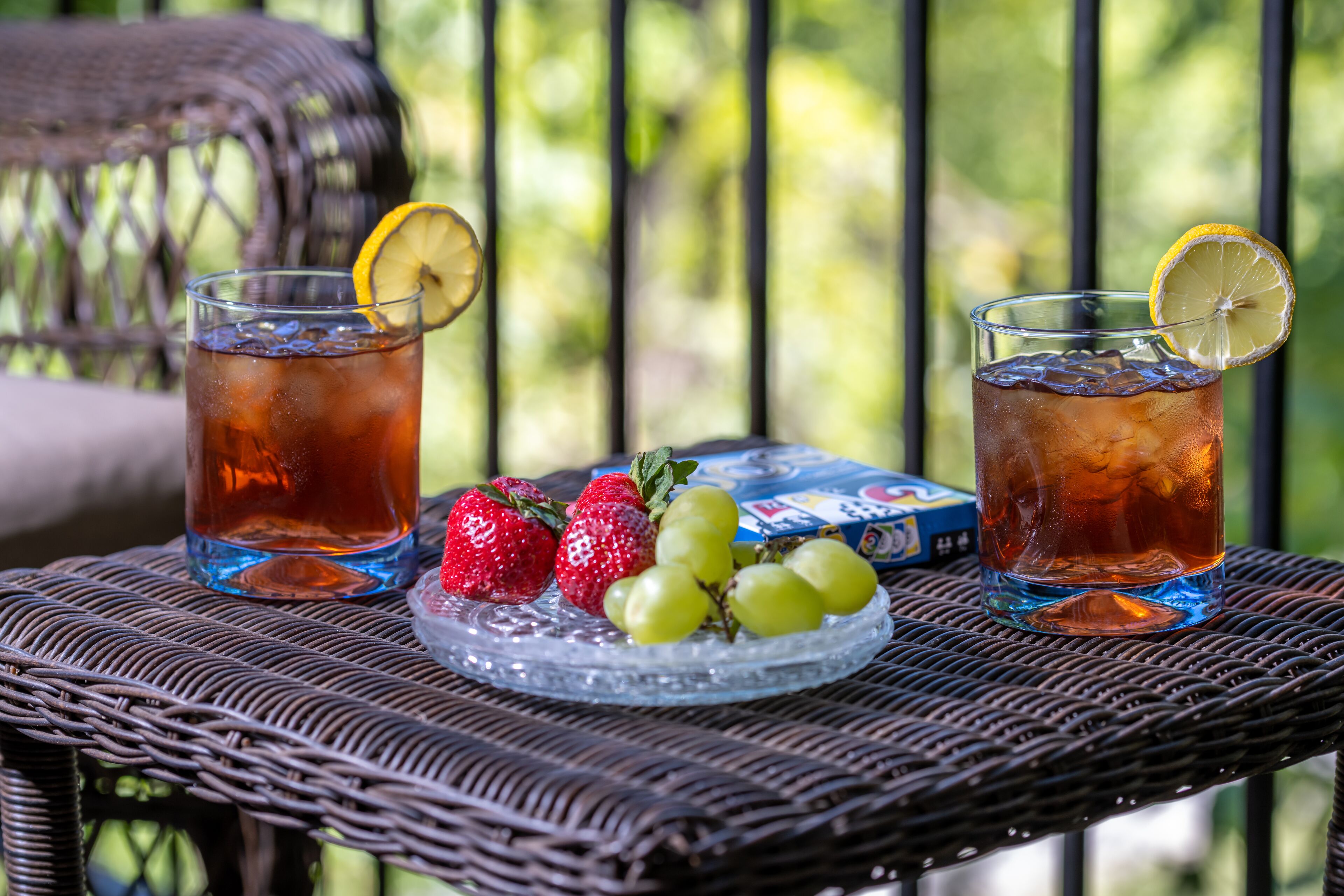 Two glasses of iced tea with lemon slices on a wicker table with strawberries and grapes.