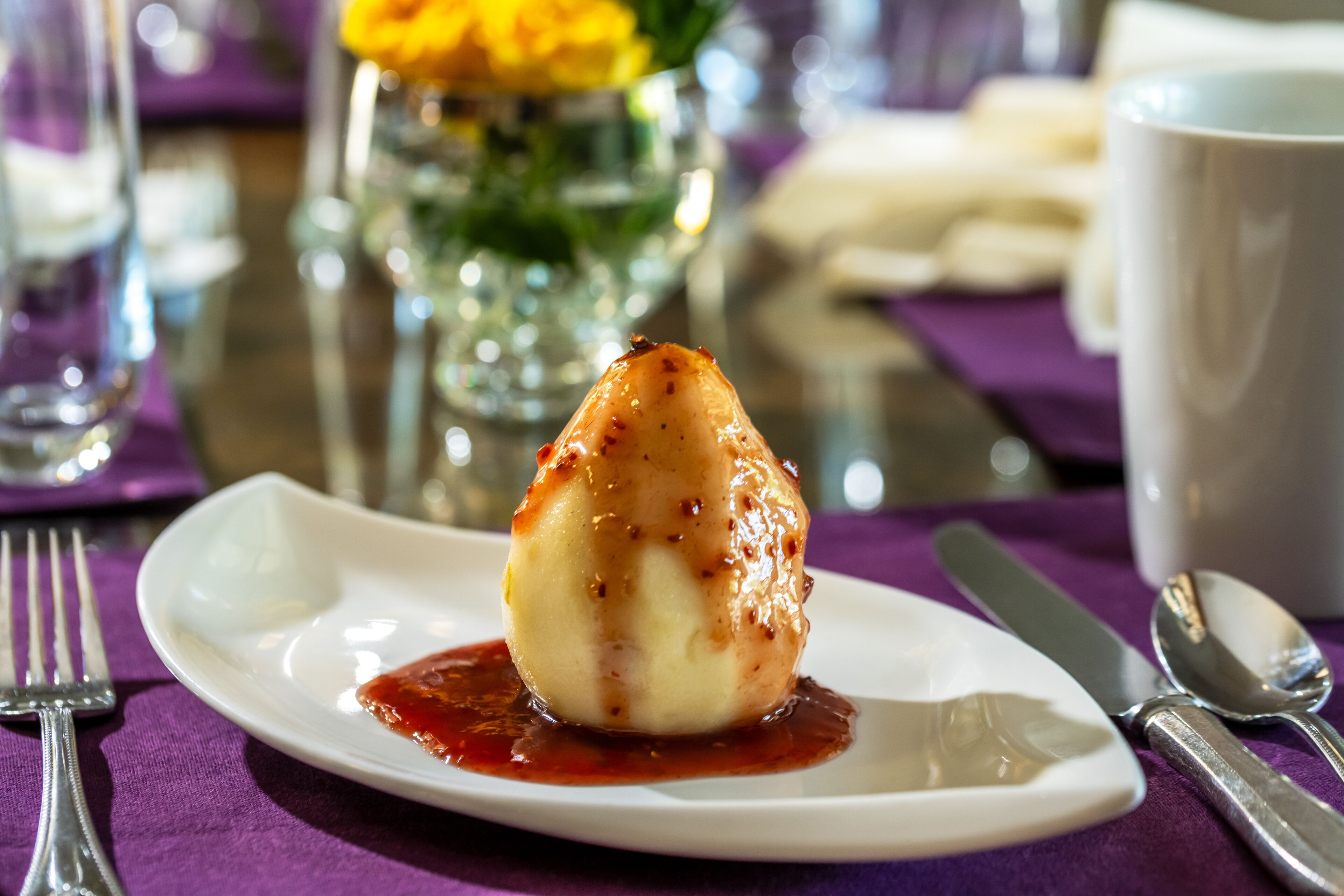 Un dessert su un piatto bianco con salsa rossa, accompagnato da posate su una tovaglia viola.