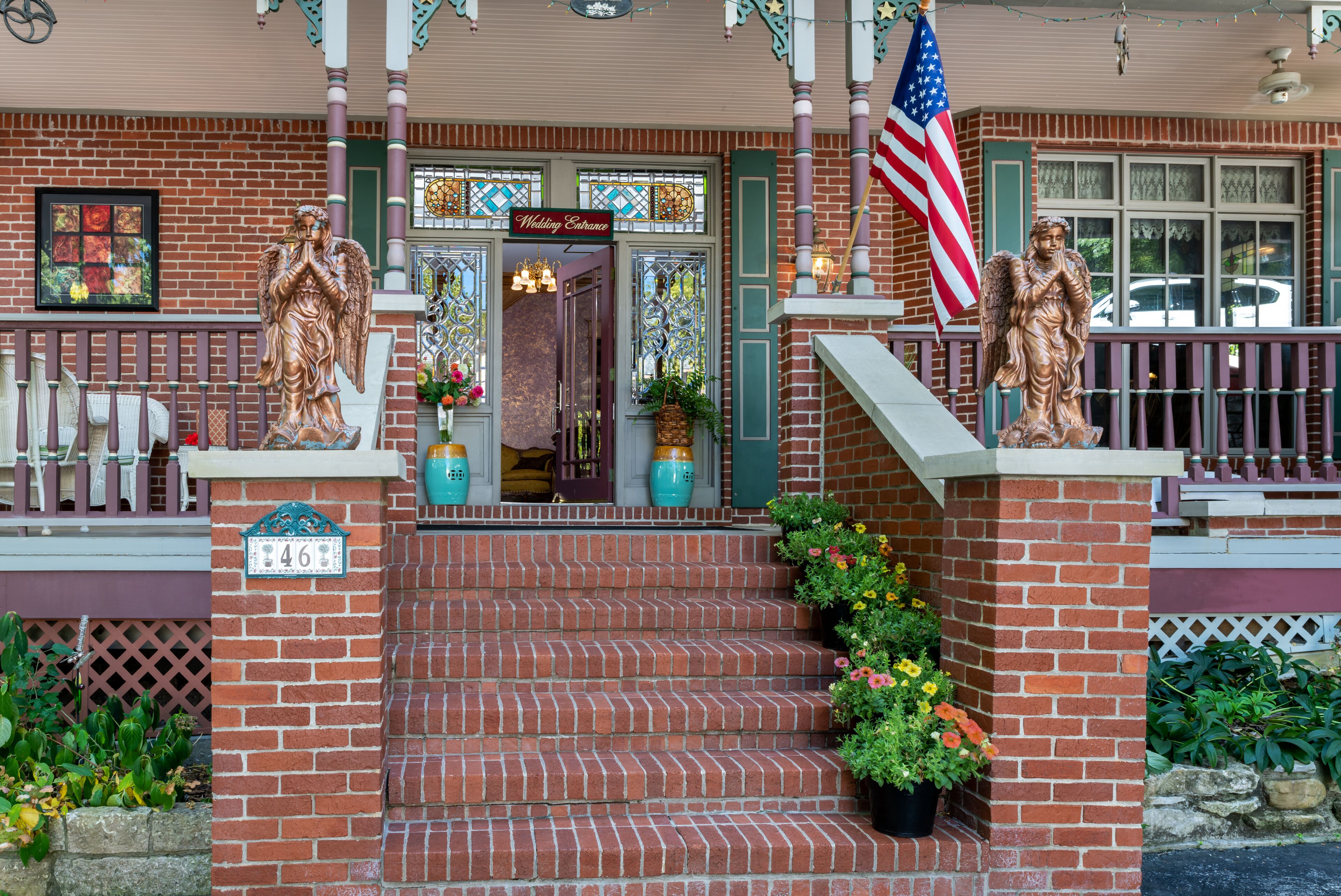 A brick building with a porch, steps, and two angel statues.
