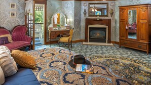 A room with a fireplace, a large rug, a sofa, a desk, and a wardrobe. - Angel At Rose Hall (Eureka Springs)
