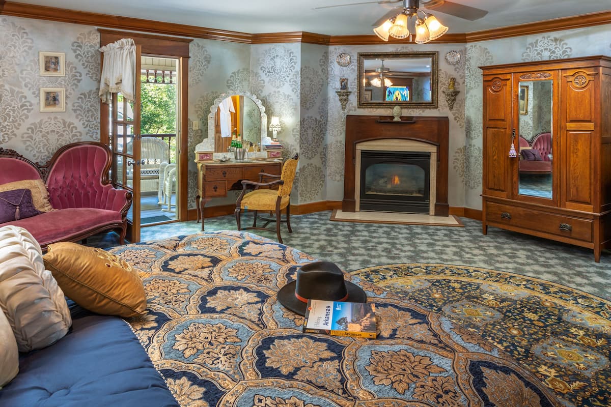 A room with a fireplace, a large rug, a sofa, a desk, and a wardrobe.