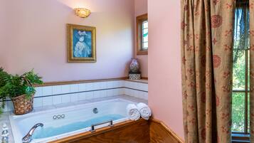 Une salle de bain avec une baignoire, un luminaire fixé au mur, un tableau encadré et une fenêtre avec des rideaux.