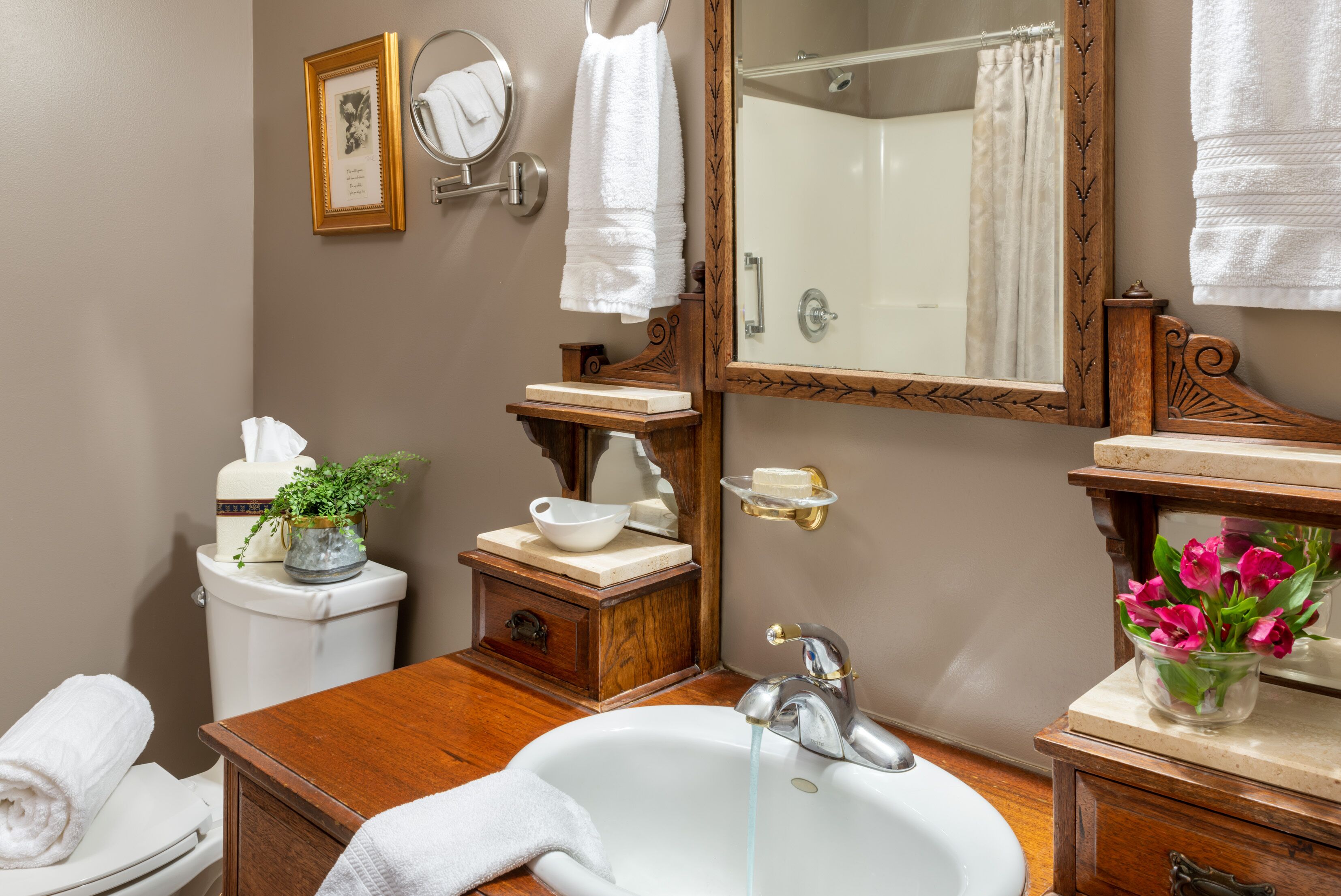 A bathroom with a white sink, wooden vanity, a mirror, a toilet, and a shower with a glass door.