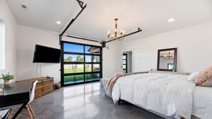 A bedroom with a large bed, a TV, a desk, and a view of a green landscape through a sliding door. - La Bella Vita (The Beautiful Life) 5+ Bedrooms (Spearfish)