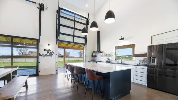 A modern kitchen with a large island, bar stools, a built-in oven, and a view of the outdoors. - La Bella Vita (The Beautiful Life) 5+ Bedrooms (Spearfish)