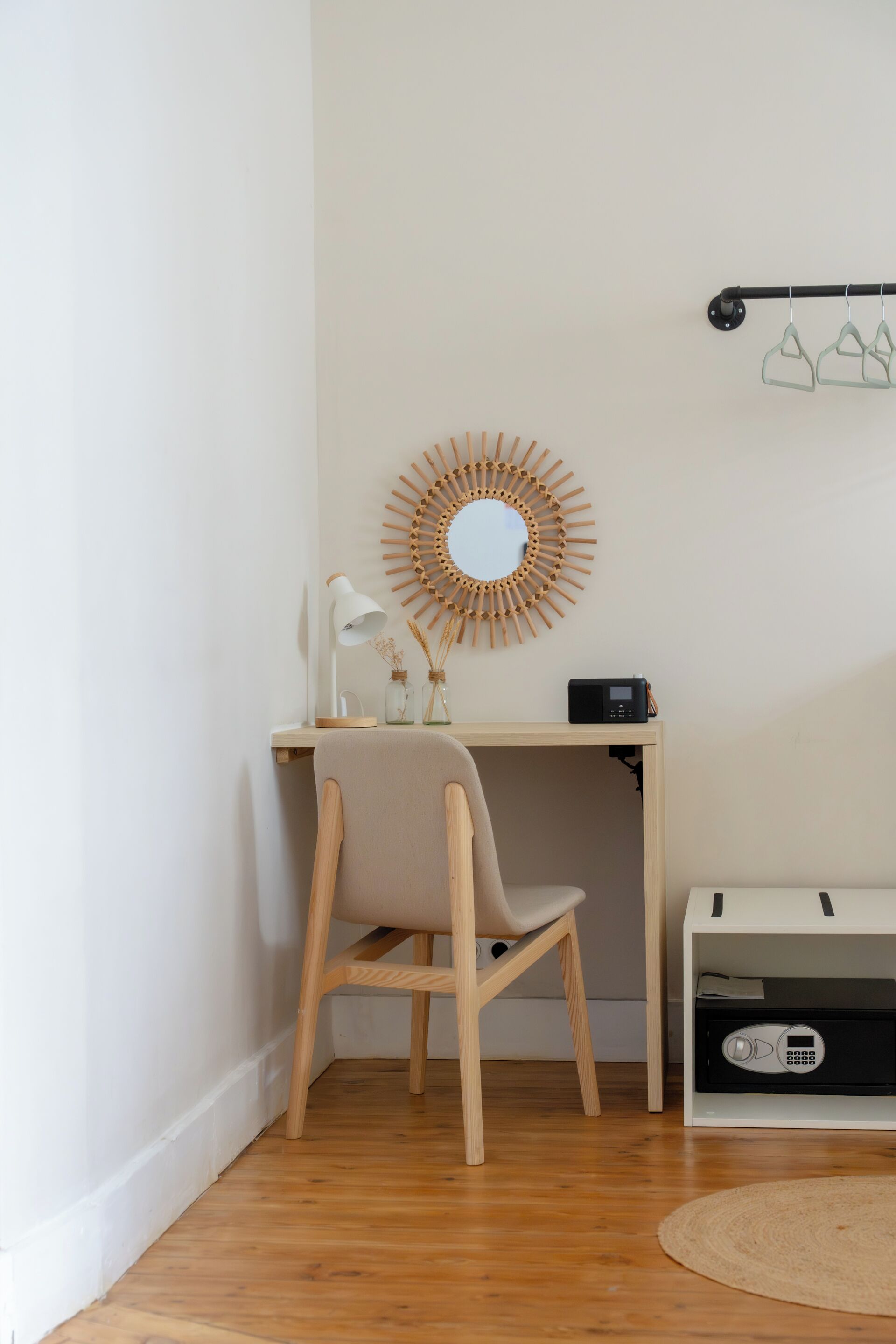 A corner room with a wooden desk, a chair, a small shelf with a radio, a decorative mirror, and a wall-mounted rack.
