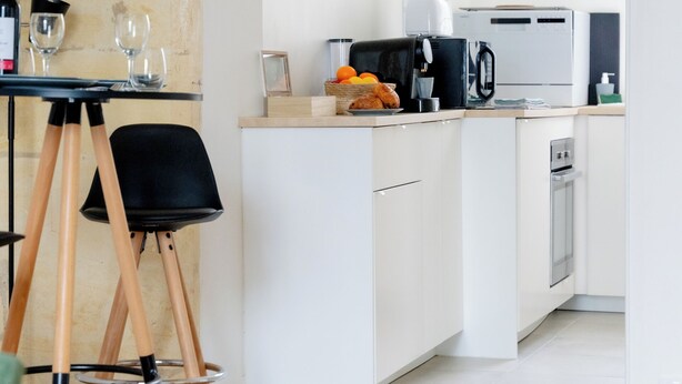 A modern kitchen with white cabinets, a black chair, and a dining table with wine glasses. - The Libournettes - Serenity (Libourne)