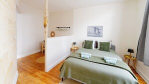 A bedroom with a bed, a chair, a small table, a lamp, and a wall art piece. - The Libournettes - Serenity (Libourne)