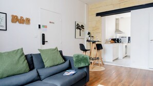 A modern living room with a grey sofa, green cushions, and a small table with chairs. A kitchen is visible in the background. - The Libournettes - Serenity (Libourne)