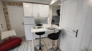 A compact kitchen with white cabinets, a built-in refrigerator, a coffee machine, and a small dining area with two stools. - Le Petit Paradis. (Brive-la-Gaillarde)