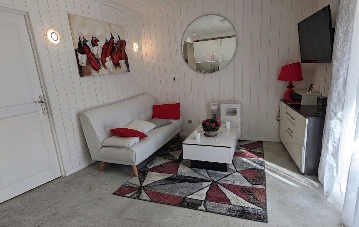 A room with a white sofa, a coffee table, a mirror, and a red lamp.
