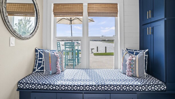 Un dormitorio con una cama estampada, un espejo grande y vistas a un área verde y un edificio a través de la ventana.
