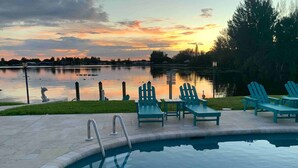 Una piscina con sillas de descanso y vistas a un lago al atardecer.