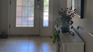 Ein Zimmer mit weißer Tür, einer Deckenleuchte, einem Blumentopf und einem Spiegel an der Wand.