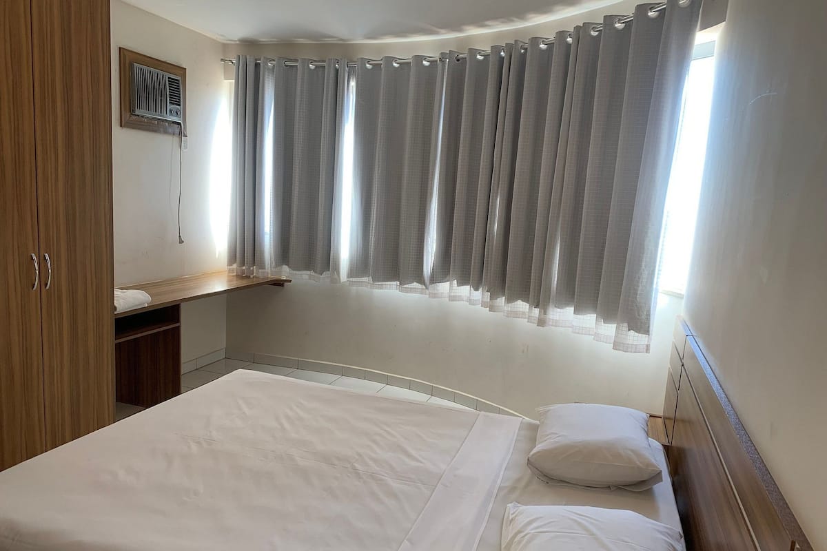 A bedroom with a bed, a wooden wardrobe, a small desk, and a window with curtains.