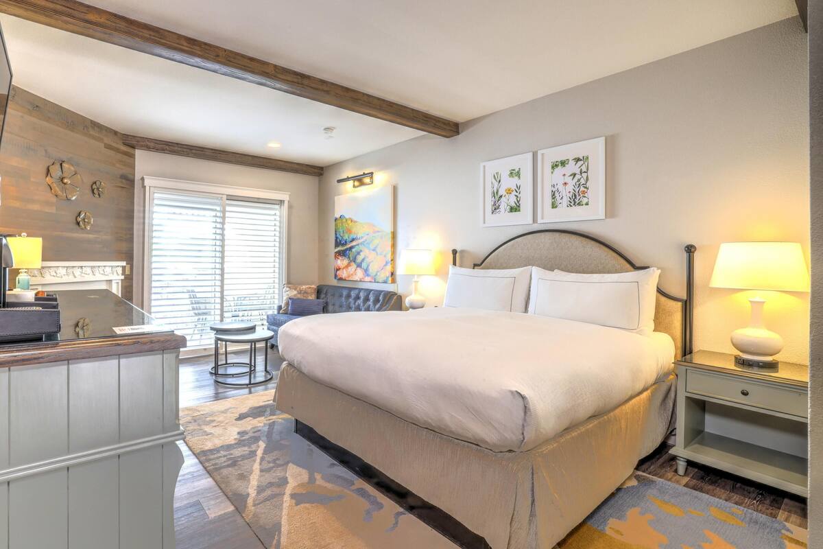 A hotel room with a large bed, a desk, a chair, a sofa, and two wall-mounted lamps.