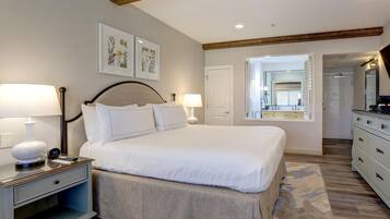 A hotel room with a bed, bedside tables, a nightstand, a mirror, and a door leading to a bathroom.