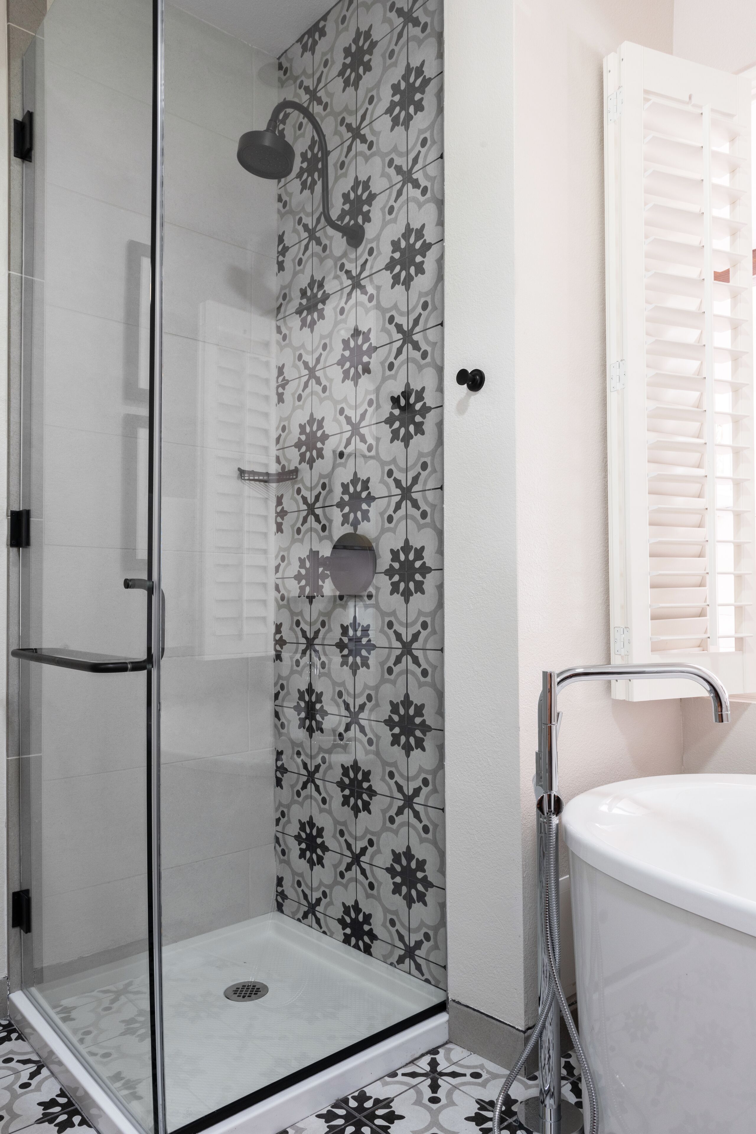 Eine Dusche mit Glastür, eine weiße Badewanne und eine Wand mit Muster.
