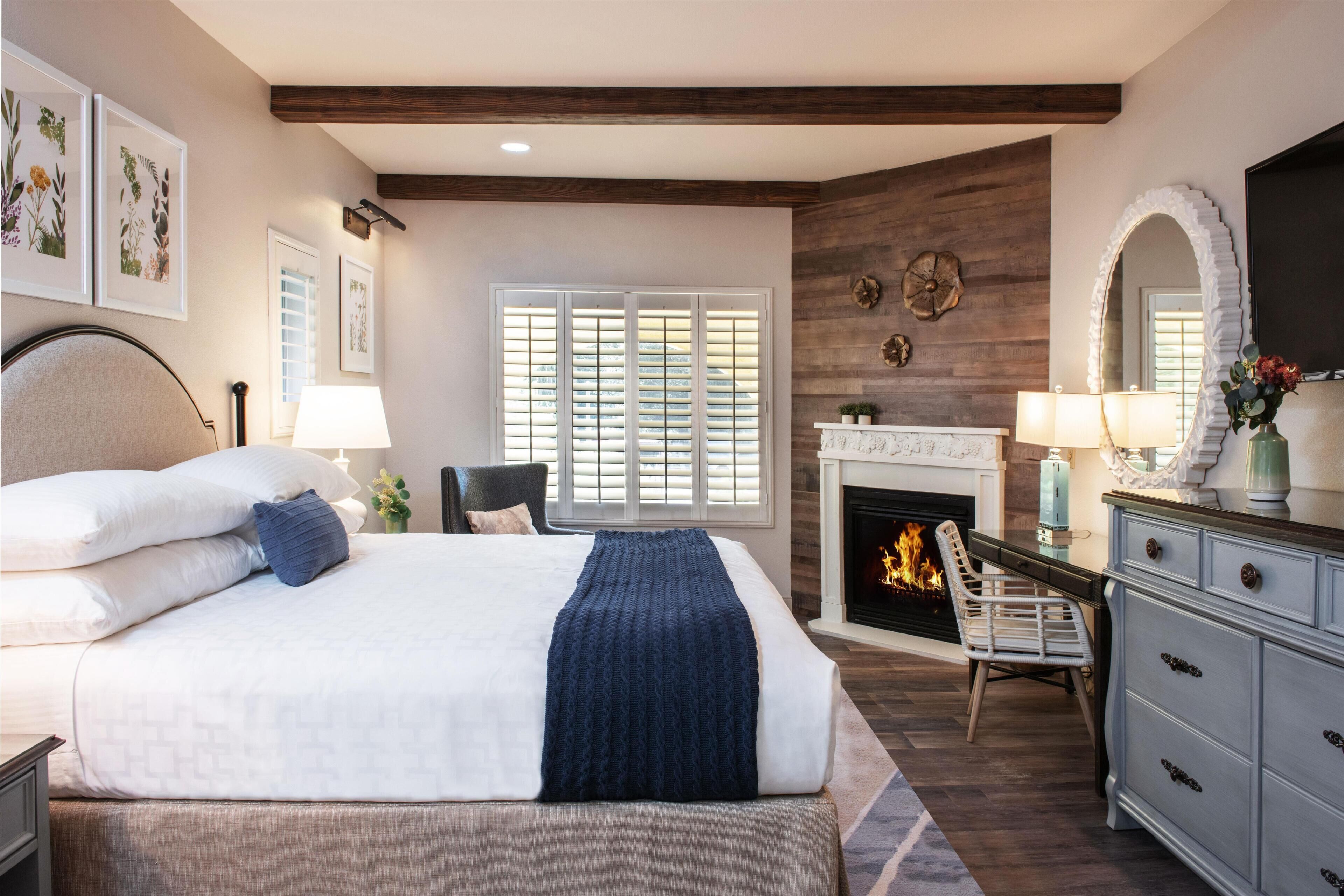 A bedroom with a bed, a fireplace, a dresser, and a chair.