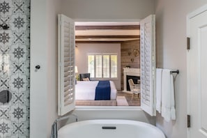 A bathroom with a bathtub, a window with blinds, and a view of a bedroom with a bed and a fireplace. - The Lodge at Healdsburg, Tapestry Collection by Hilton (Healdsburg)