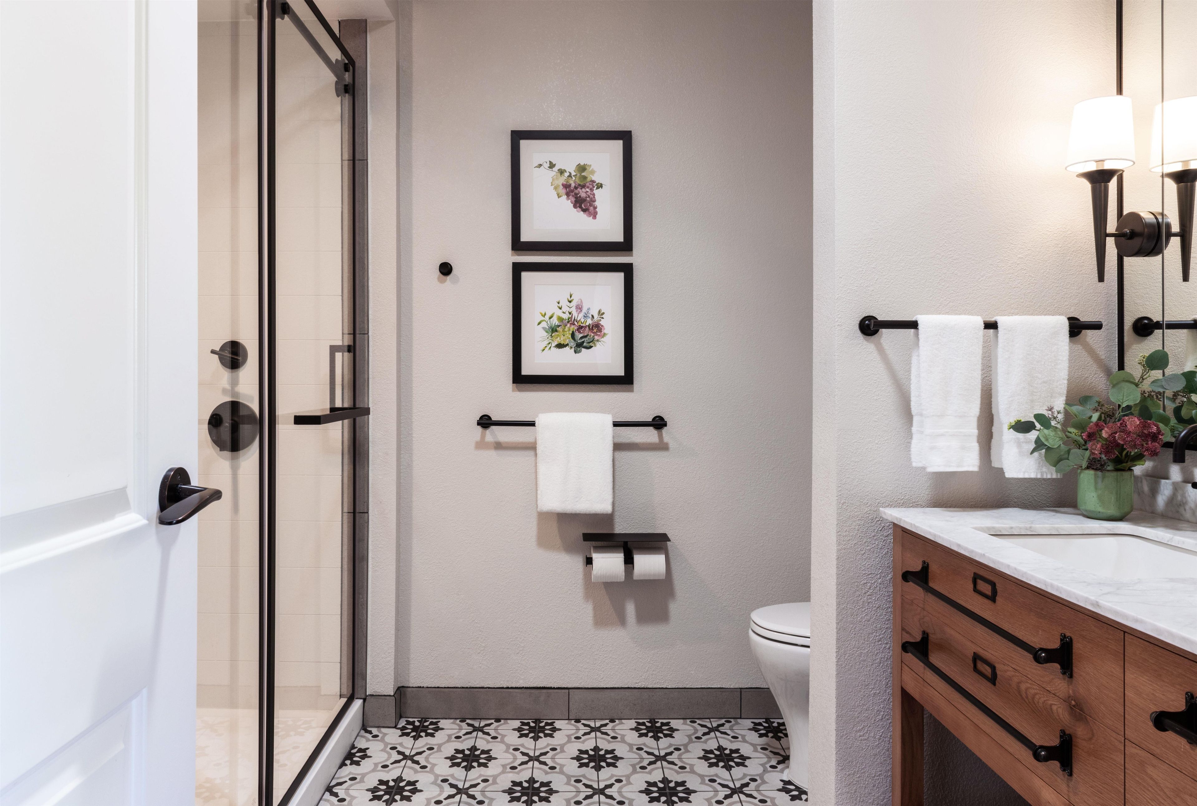 Un baño con ducha, inodoro, cuadros florales enmarcados, un perchero y un tocador con espejo.