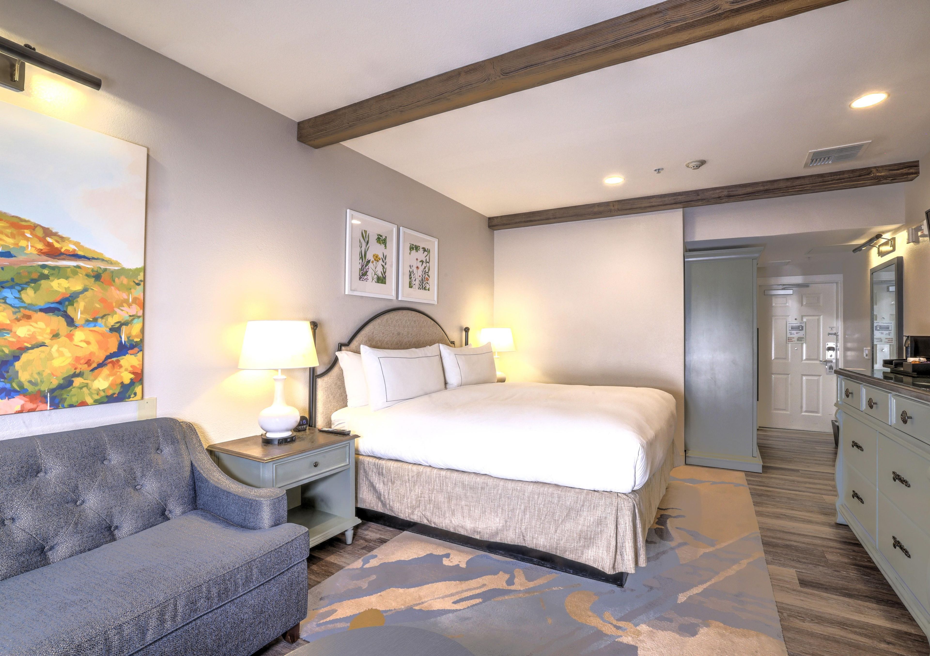 A hotel room with a bed, bedside tables, a chair, a painting, and a dresser.