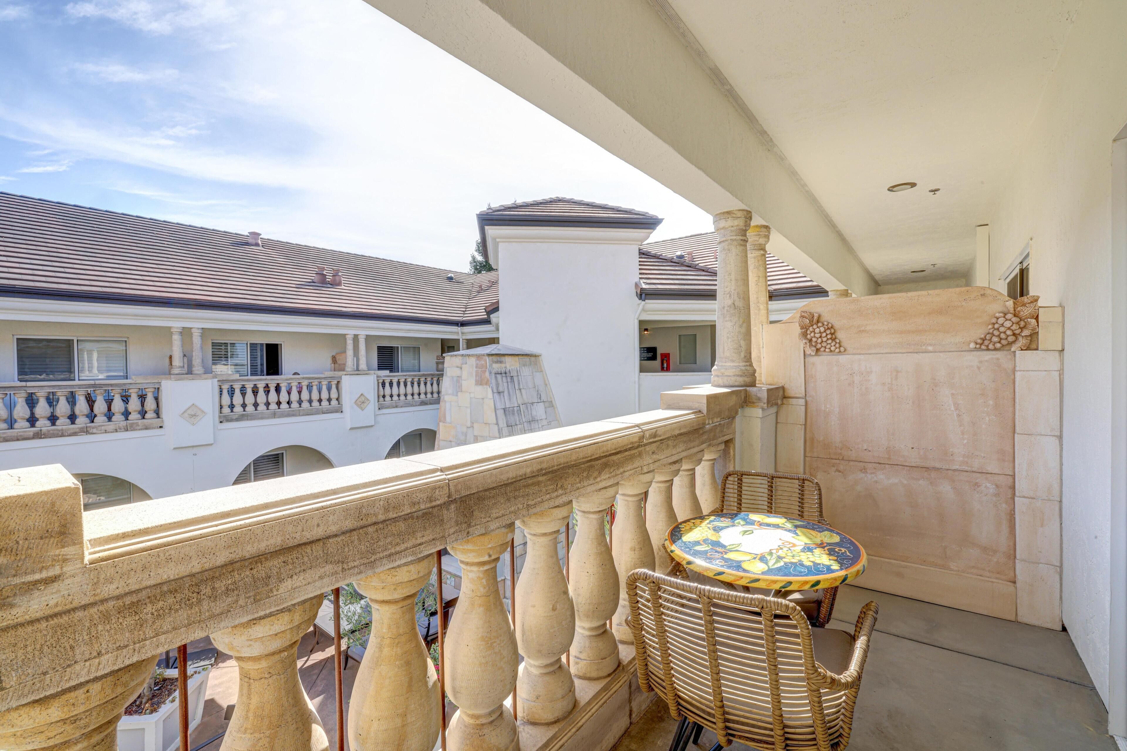 A balcony with a round table and wicker chairs, overlooking a building with a tiled roof.