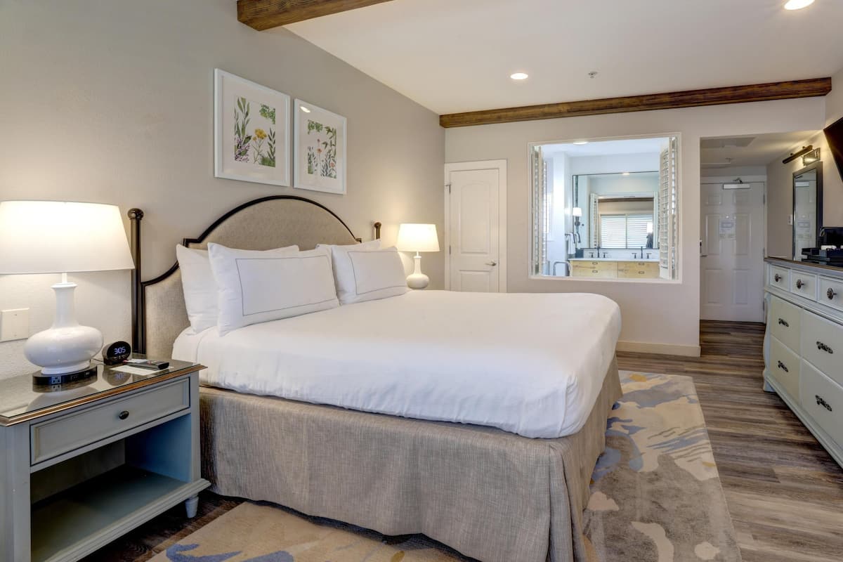 A bedroom with a bed, bedside tables, a nightstand, a mirror, and a door leading to a bathroom.