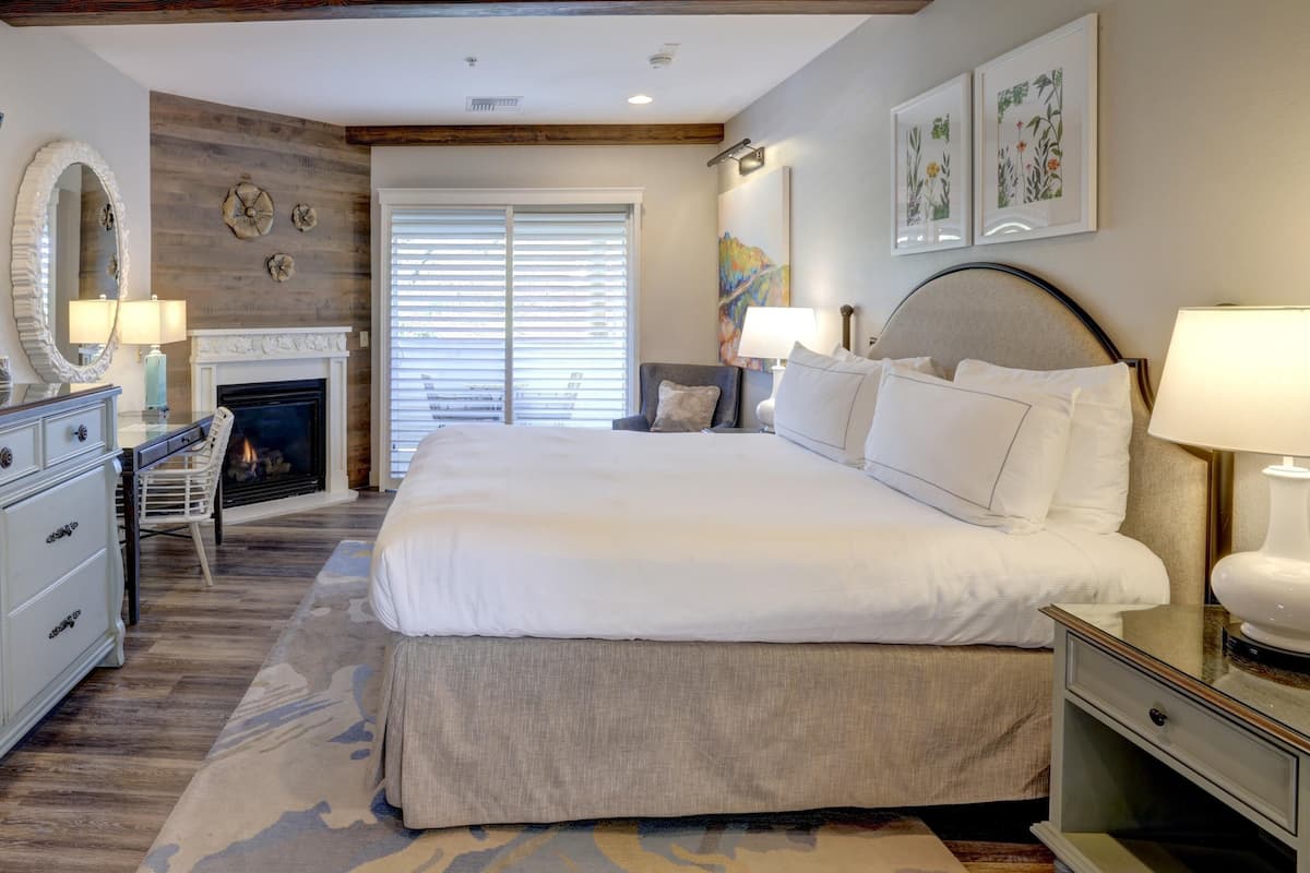 A bedroom with a large bed, a fireplace, a desk, and a chair.