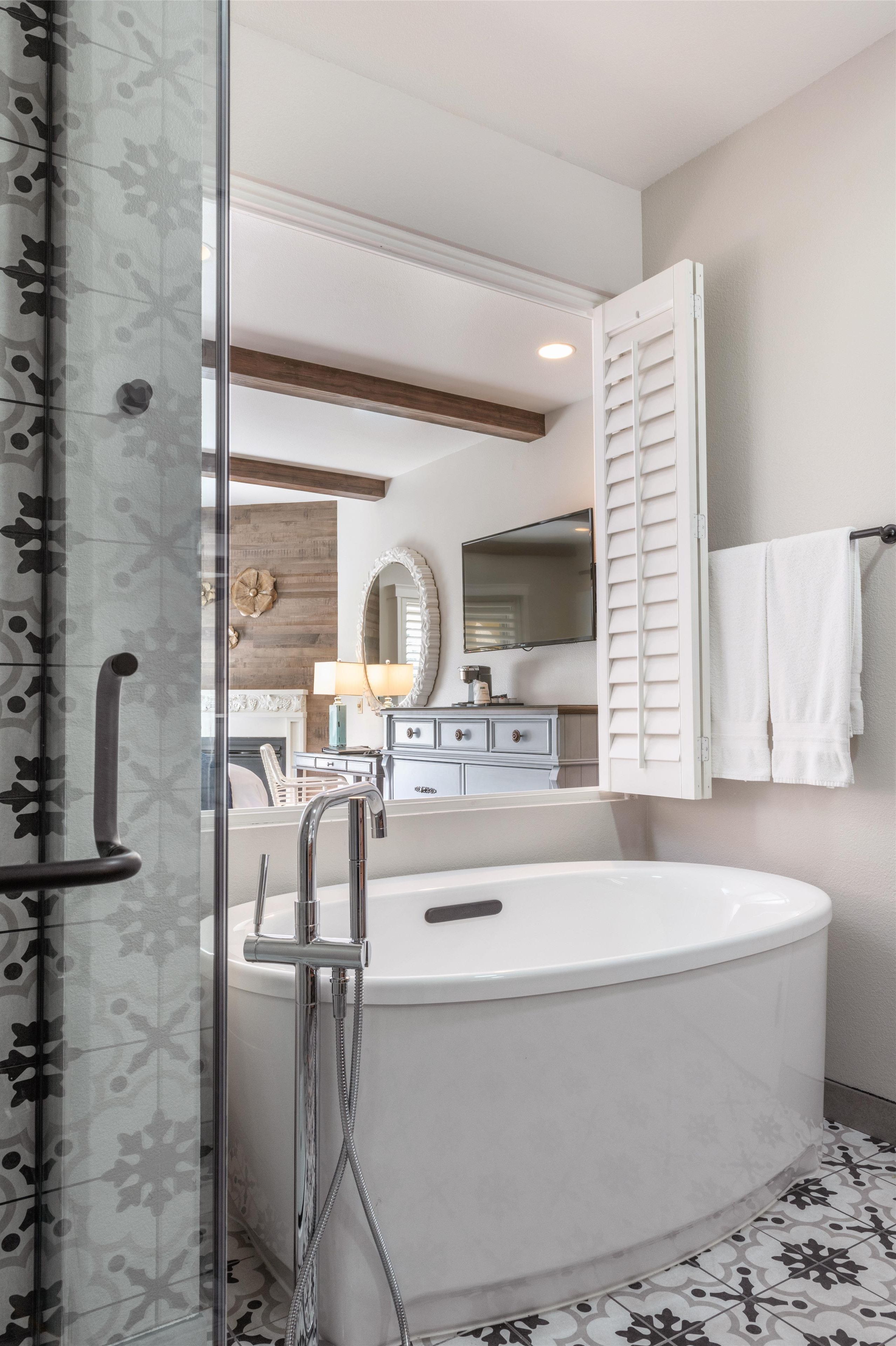 A modern bathroom with a glass shower enclosure, a freestanding bathtub, a vanity with a mirror, and a towel rack.