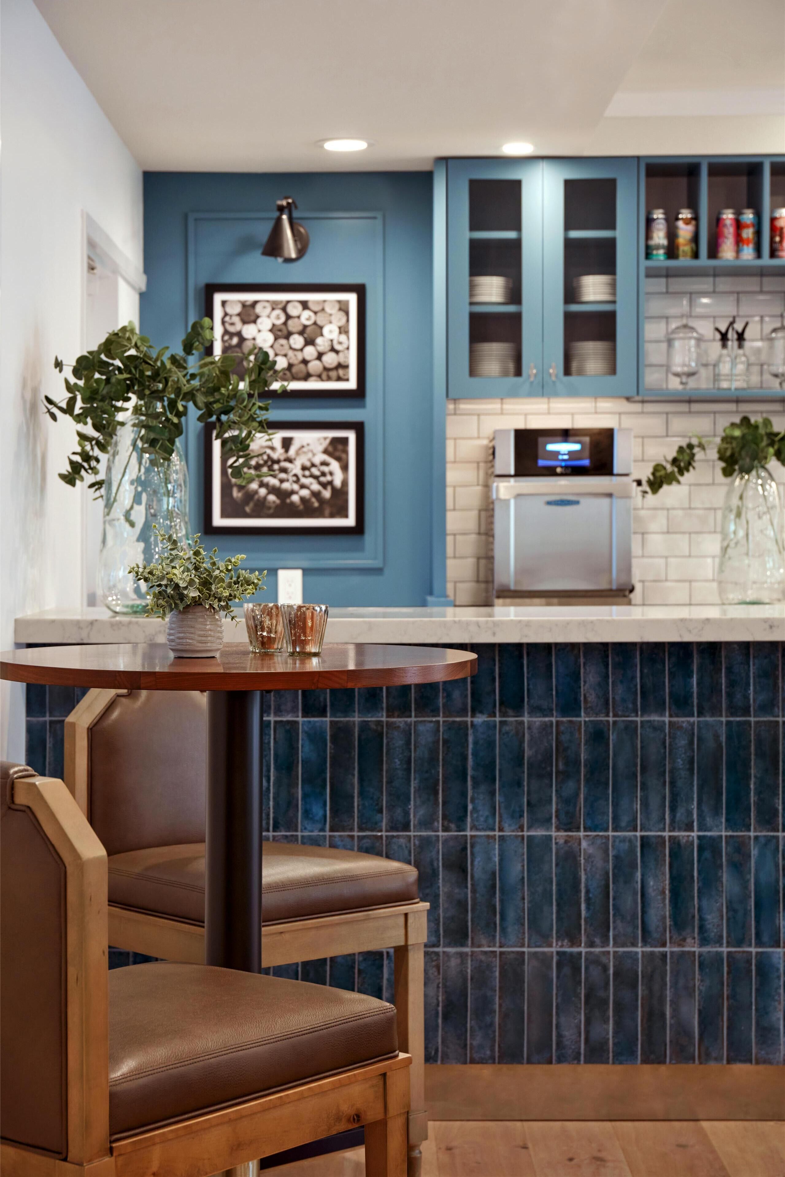 A kitchen with blue cabinets, a stainless steel refrigerator, and a wooden table with chairs.