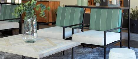 A reception area with a sign, a vase with flowers, green upholstered chairs, a table, and a patterned carpet.