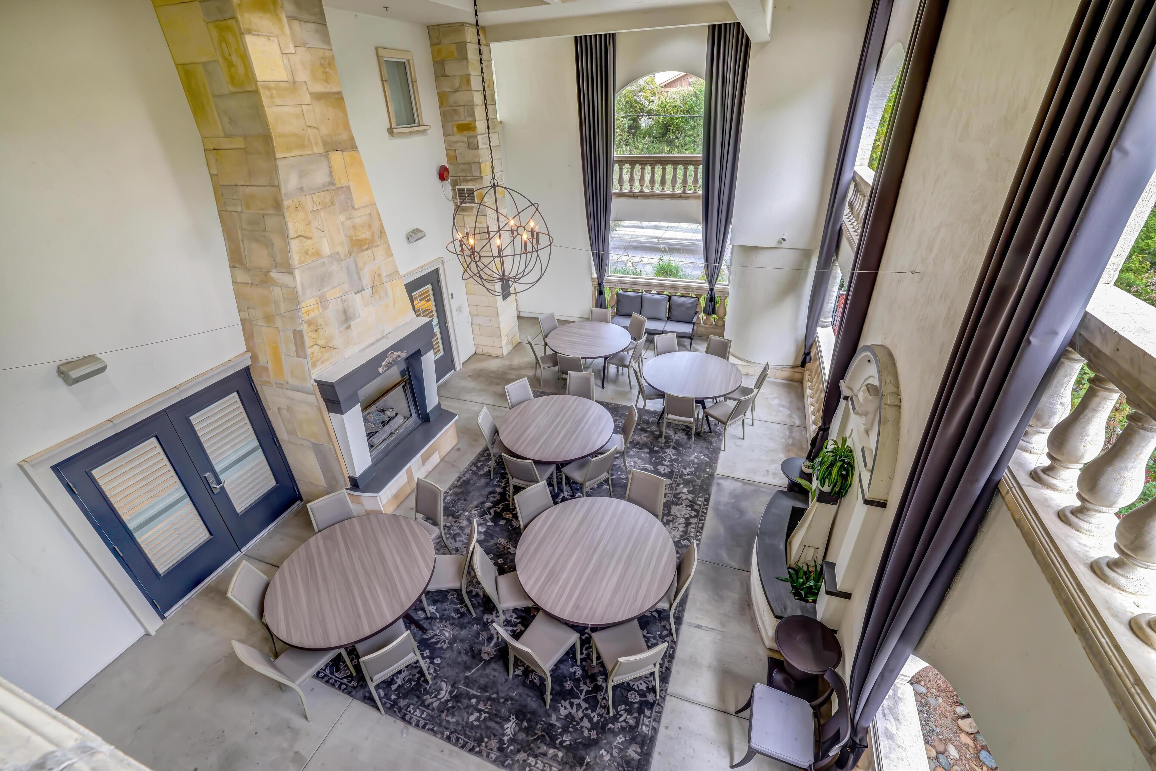 A patio area with multiple round tables and chairs, a stone fireplace, and a view of the outdoors.