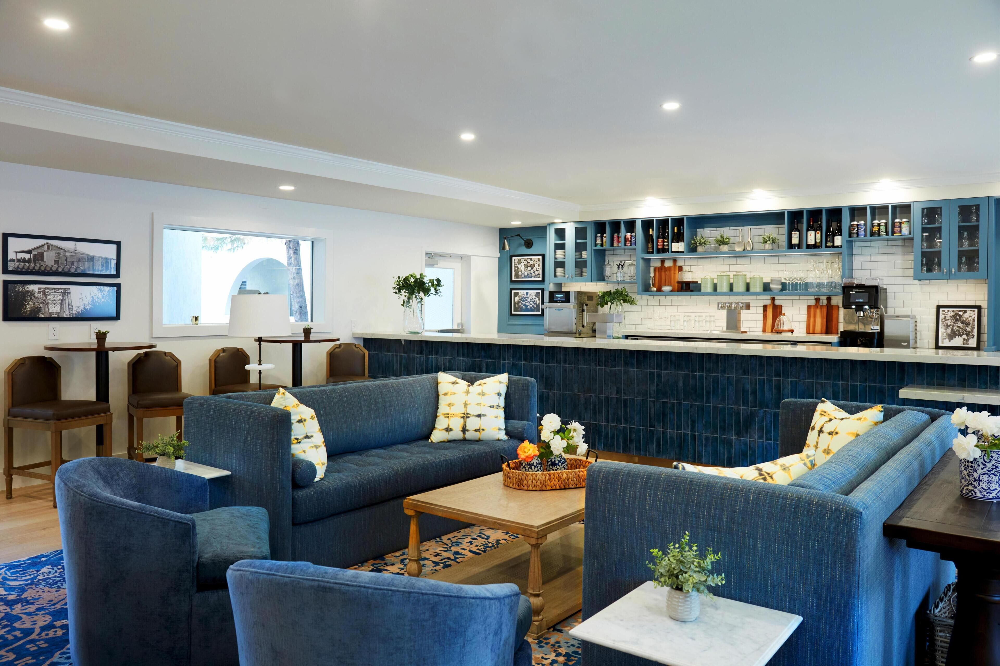 Una sala de estar moderna con sofás azules, una mesa de centro y una cocina con armarios azules y encimera blanca.