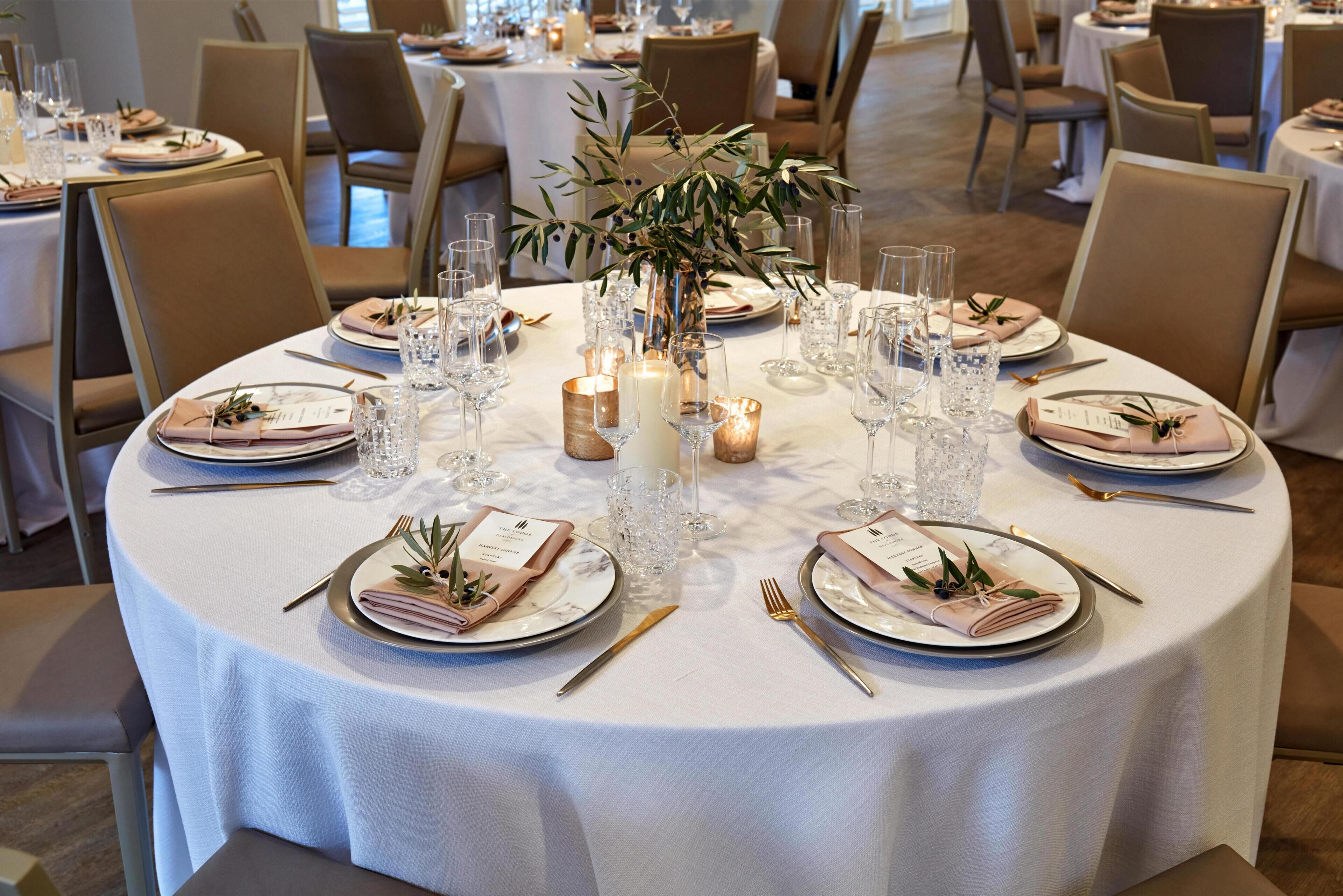 Una mesa redonda de comedor con mantel blanco, servida con platos, cubiertos y velas.