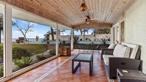 Eine überdachte Terrasse mit Pool, Gartenmöbeln und Blick auf den Pool.
